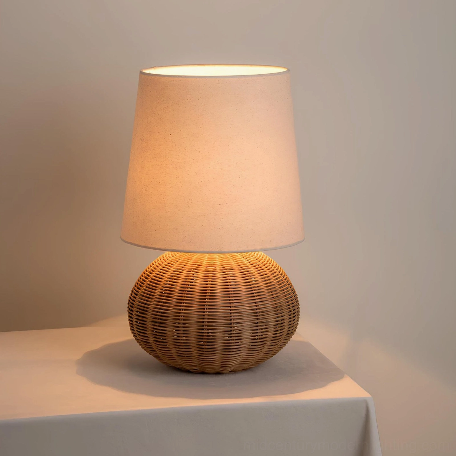 Lit Stellan rattan table lamp glowing with warm light, showcasing fabric shade illumination and woven rattan base texture