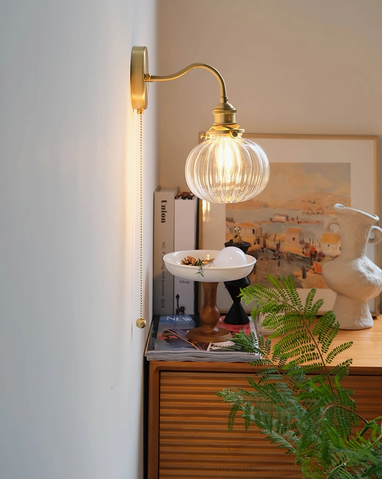Ribbed glass brass wall sconce styled with art print and green plants - mid-century modern interior design