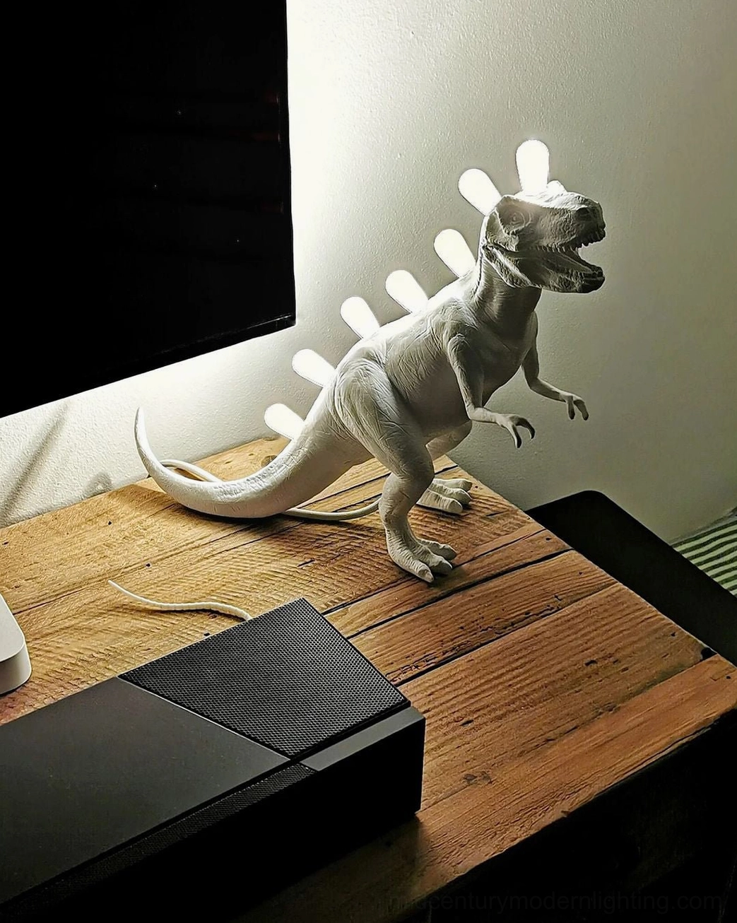 T-Rex dinosaur table lamp with dark matte finish, positioned beside computer on home office desk