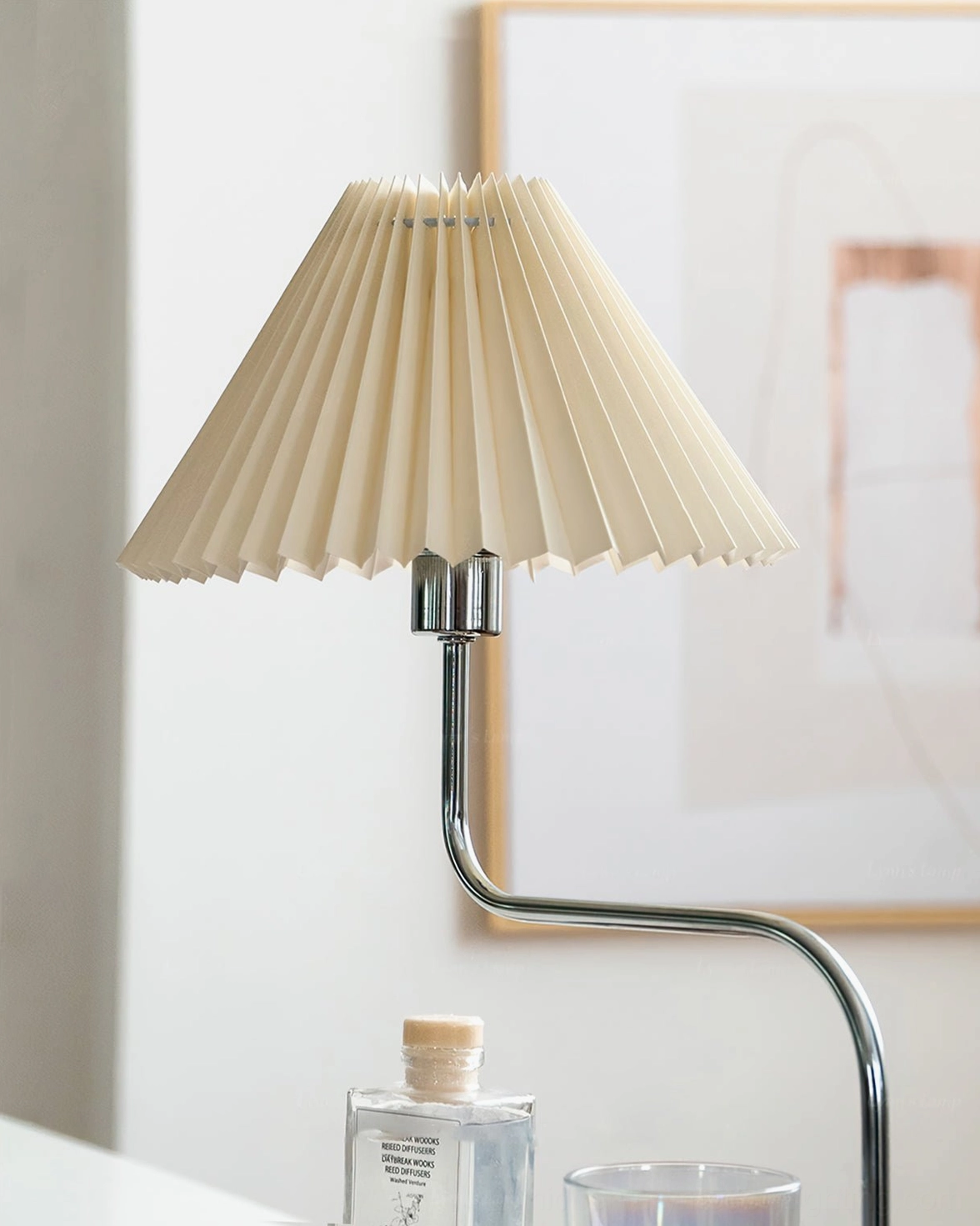 Low angle view of modern table lamp with wide pleated shade and S-curved chrome arm against wall art