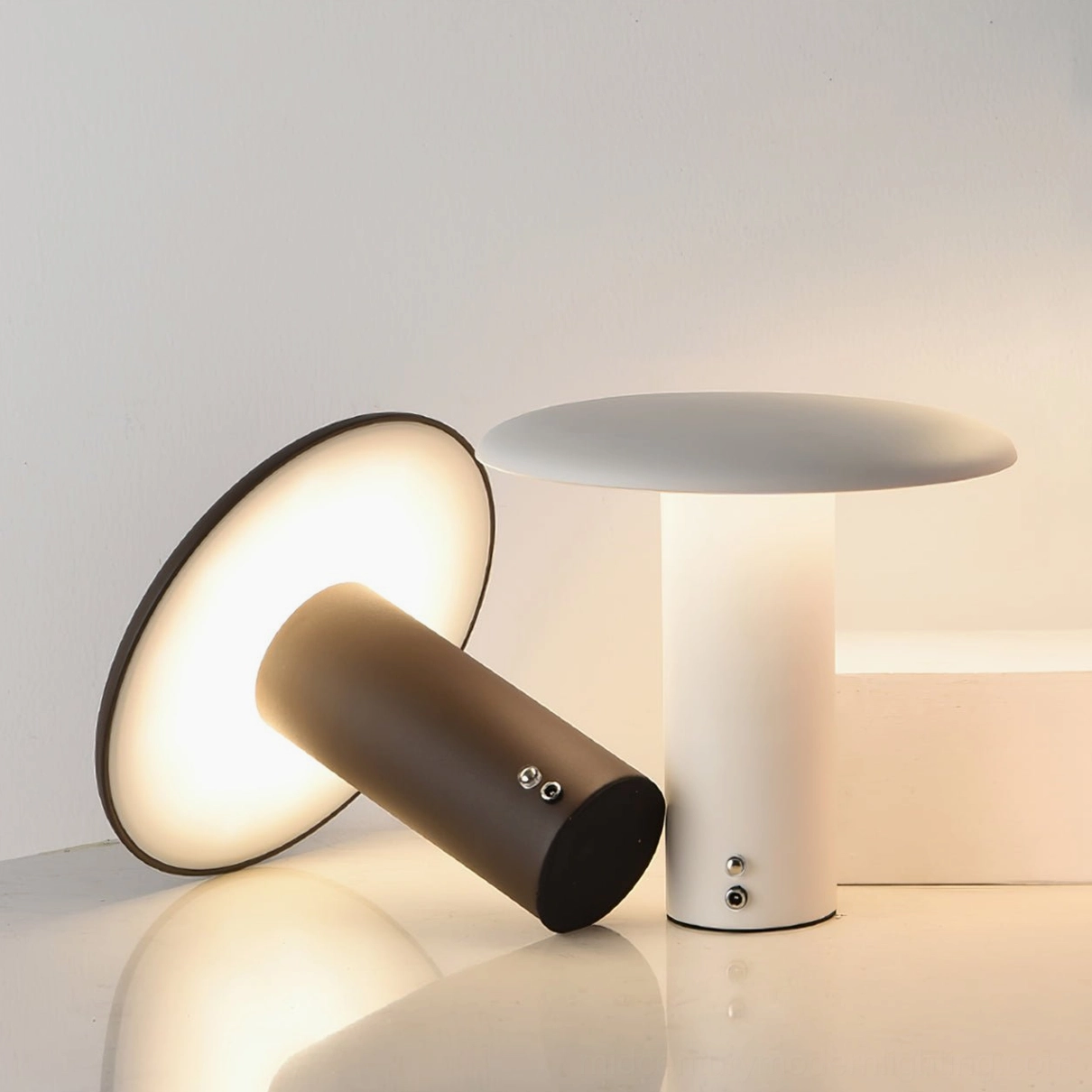 Two Takku cordless mushroom table lamps in different finishes on glossy white desktop showing color options