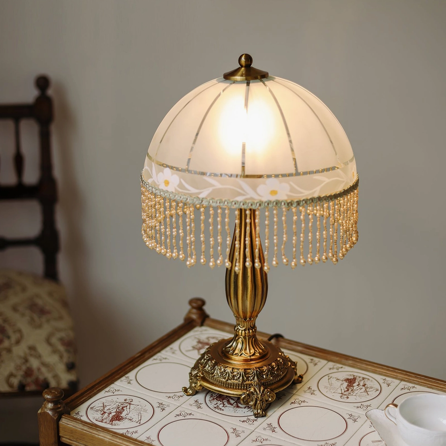 Close-up detail of carved brass base and floral patterned frosted glass shade with beaded tassel fringe