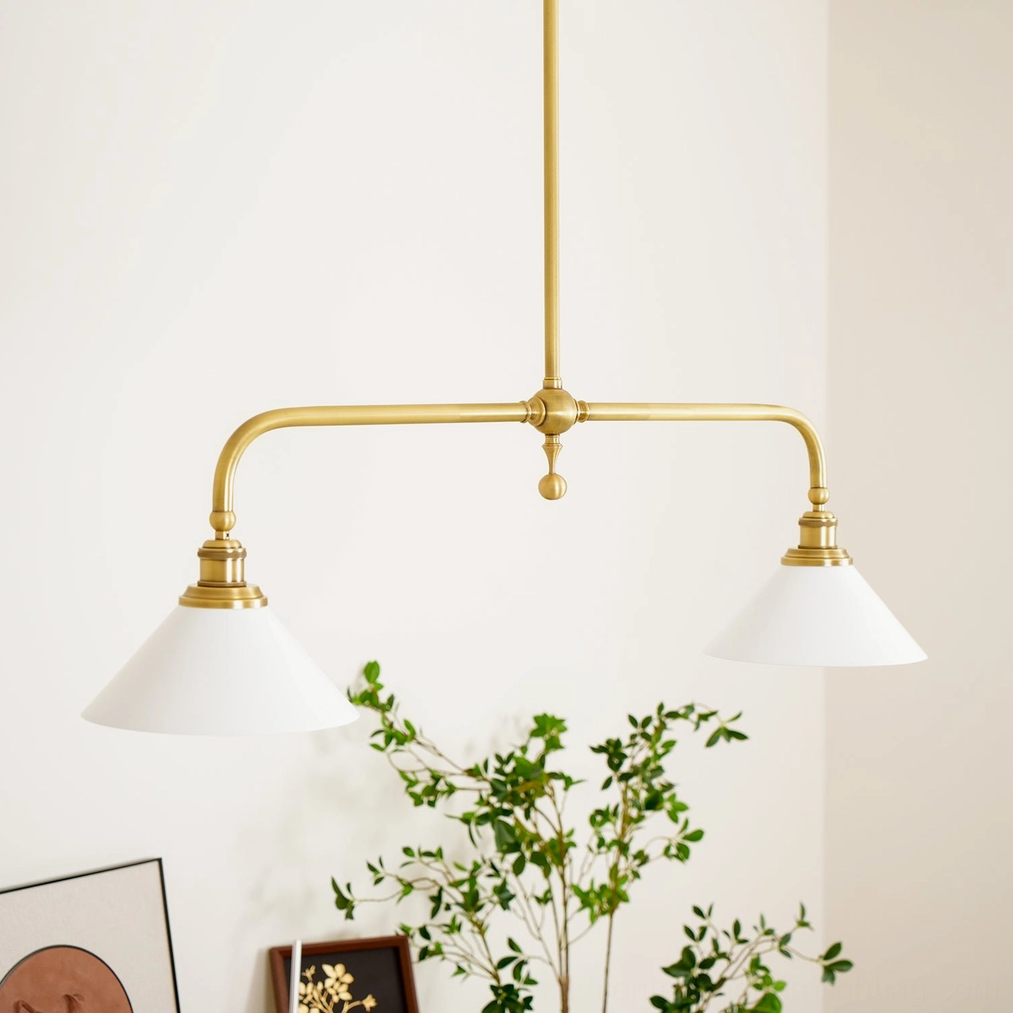 Dual-arm brass chandelier with conical white shades in minimalist home decor setting, featuring antique brass frame with potted plant styling accents