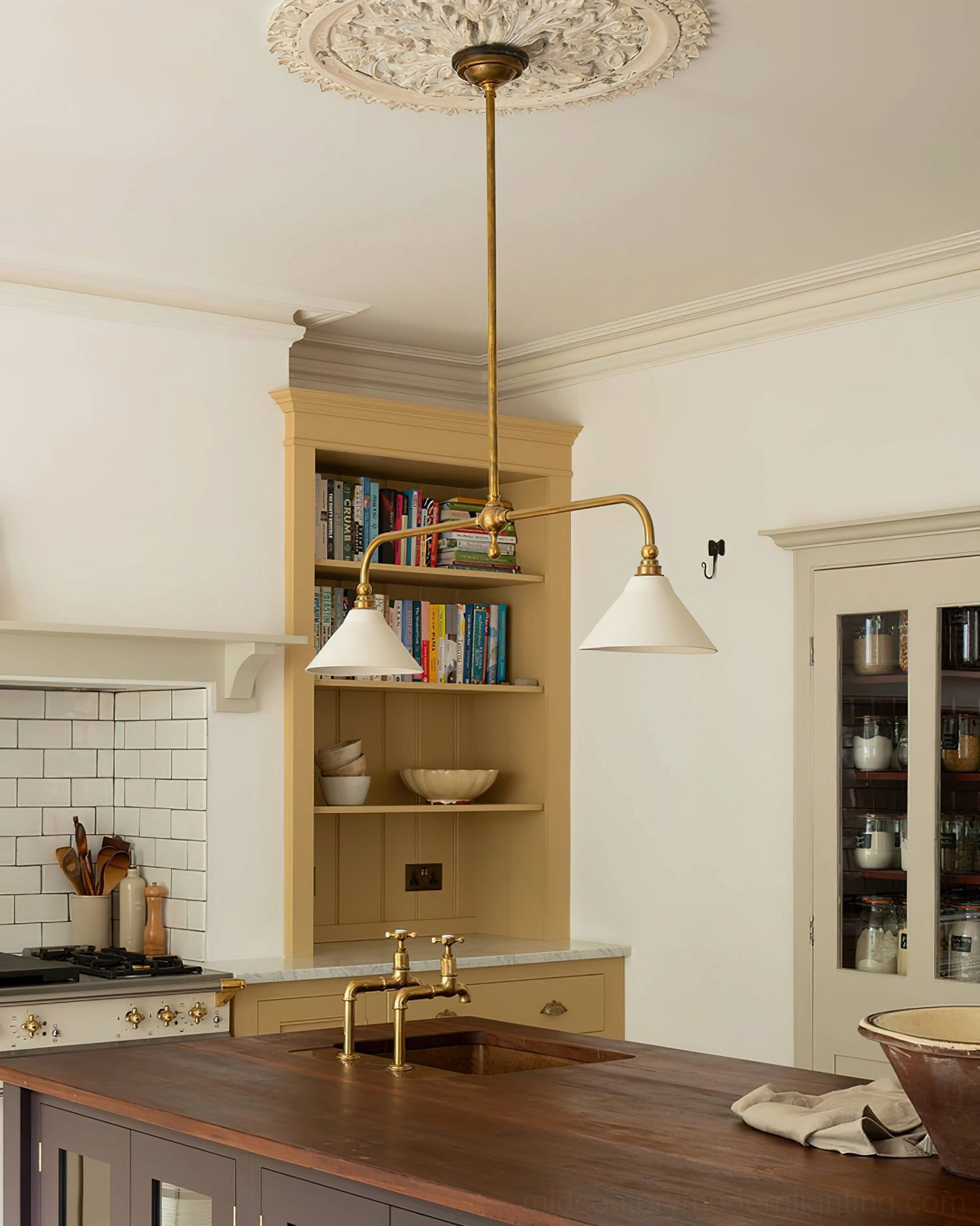 Linear two-arm brass chandelier suspended in traditional kitchen with wooden countertops, demonstrating warm brass finish and white lampshade aesthetic