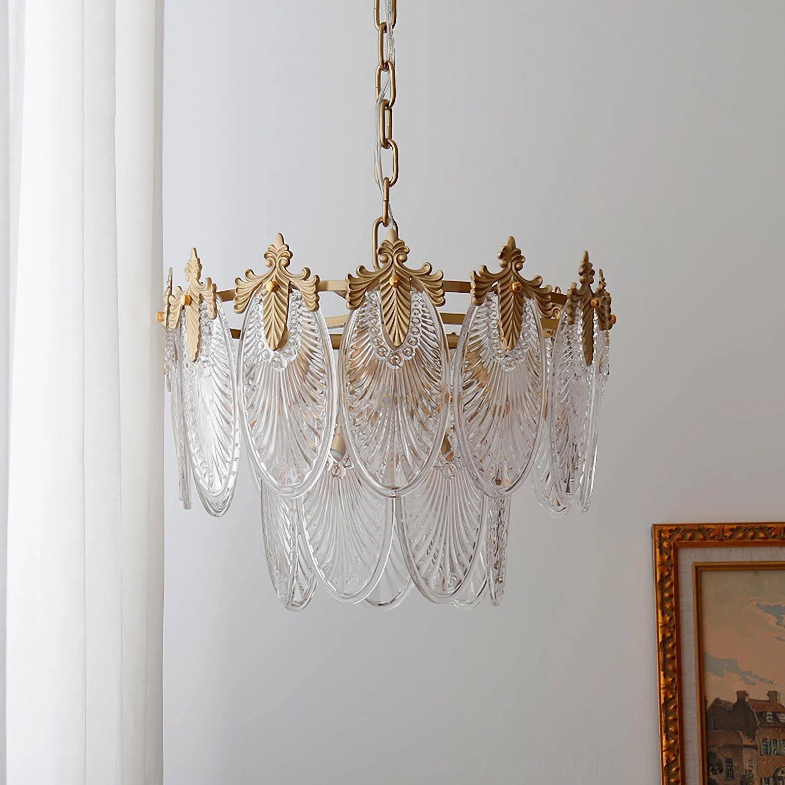 Three-tier brass chandelier unlit in interior room with framed artwork, showing polished gold brass finish and shell-ribbed glass design