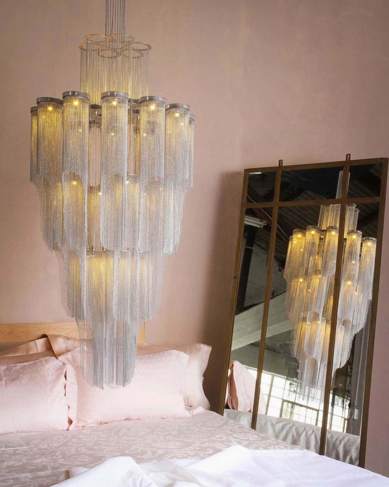 Luxury tiered crystal chandelier creating ambient lighting in upscale pink-toned bedroom