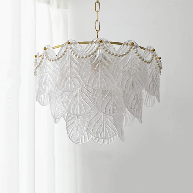 Front-facing tiered leaf glass pendant chandelier with brass chain and pearl trim in bright interior with sheer curtains, mid-century modern minimalist style