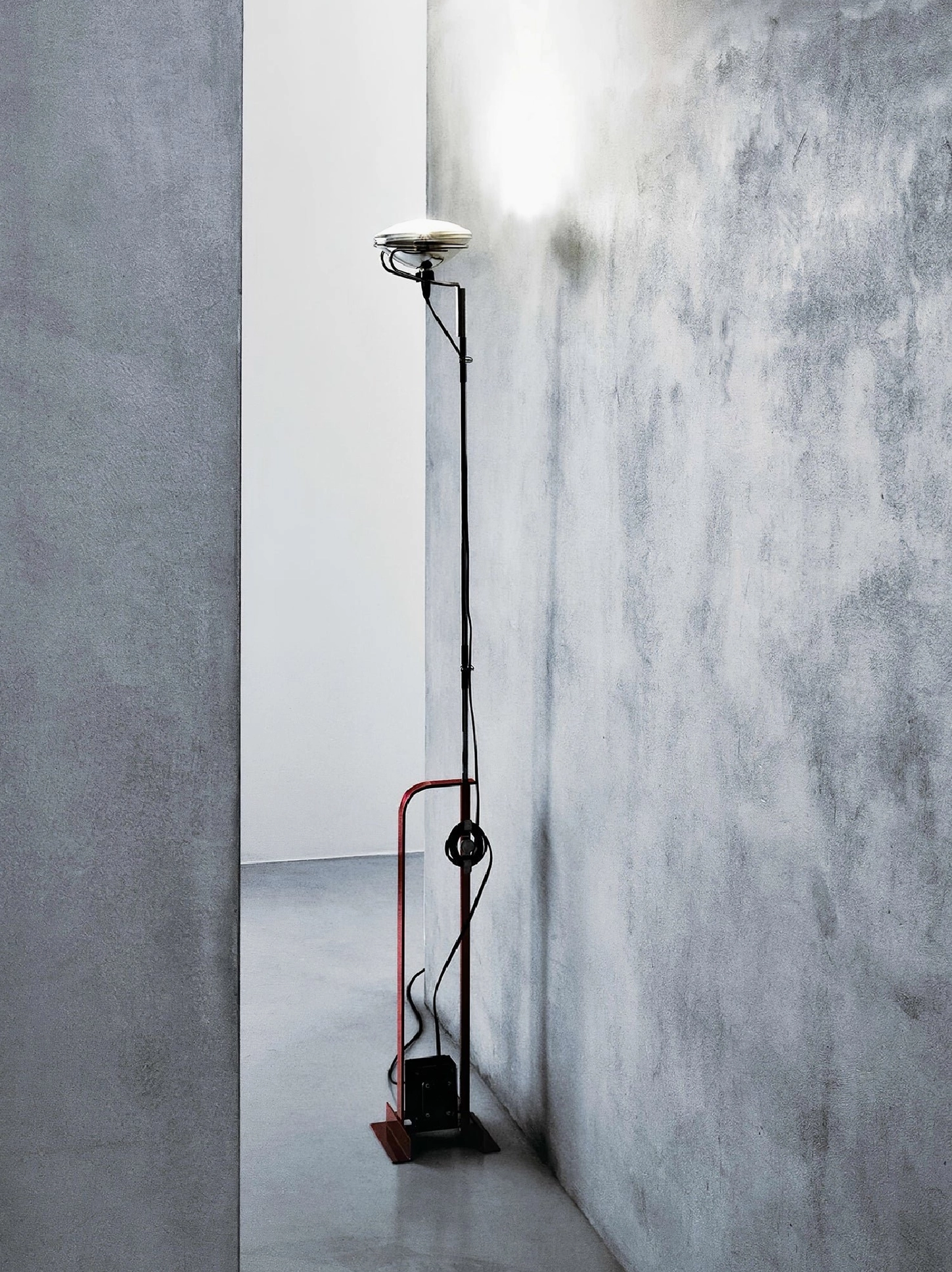 Toio red industrial floor lamp concrete wall hallway with exposed cord and warm lighting