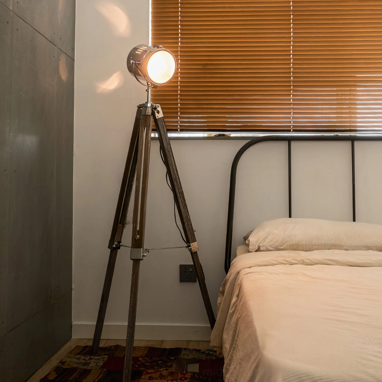 Mid-century modern tripod floor lamp positioned in vintage bedroom with iron bed, warm LED lighting casting shadows on weathered wood tripod legs