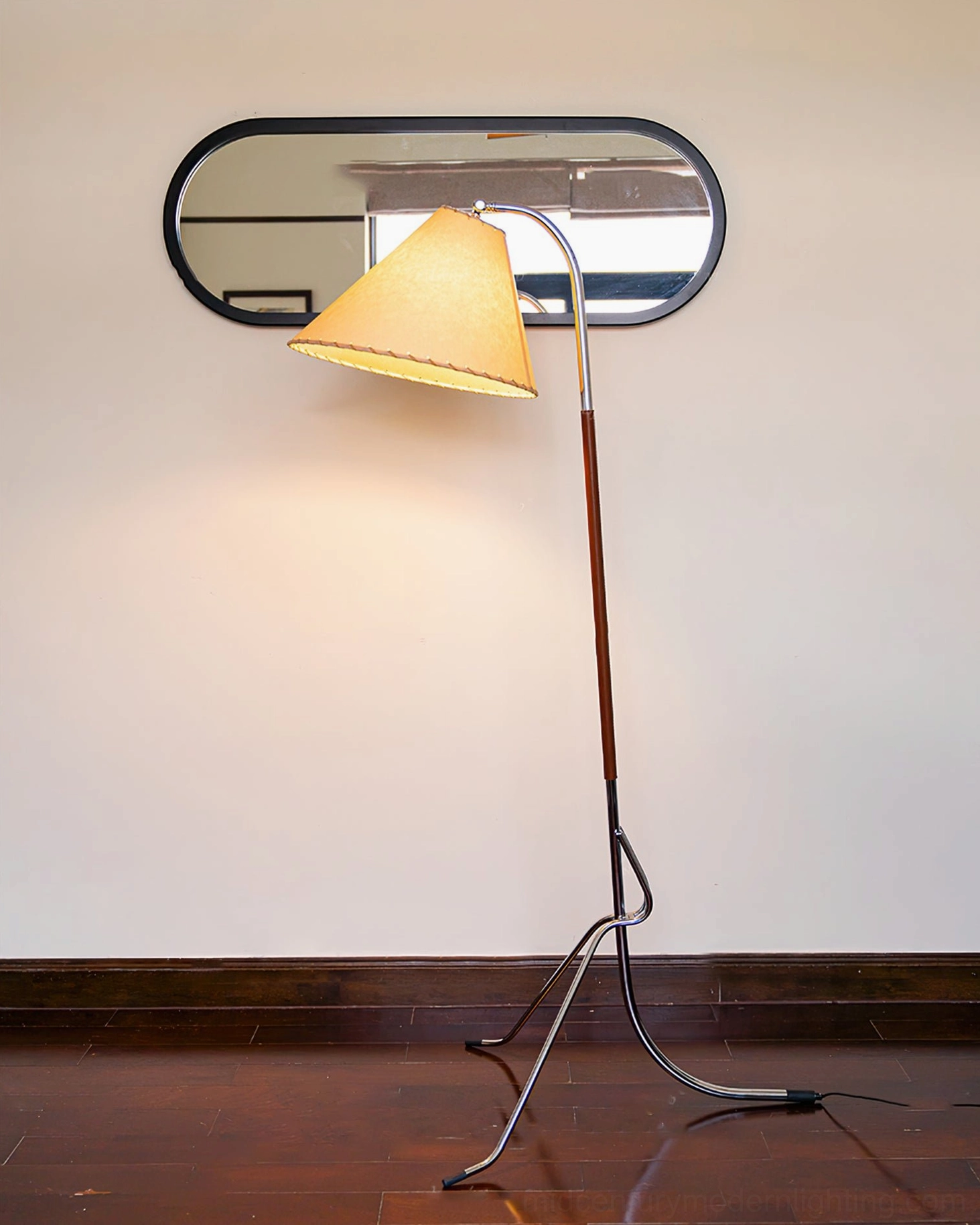 Tripod floor lamp in minimalist hallway with reflection visible in oval wall mirror, creating artistic ambient lighting effect