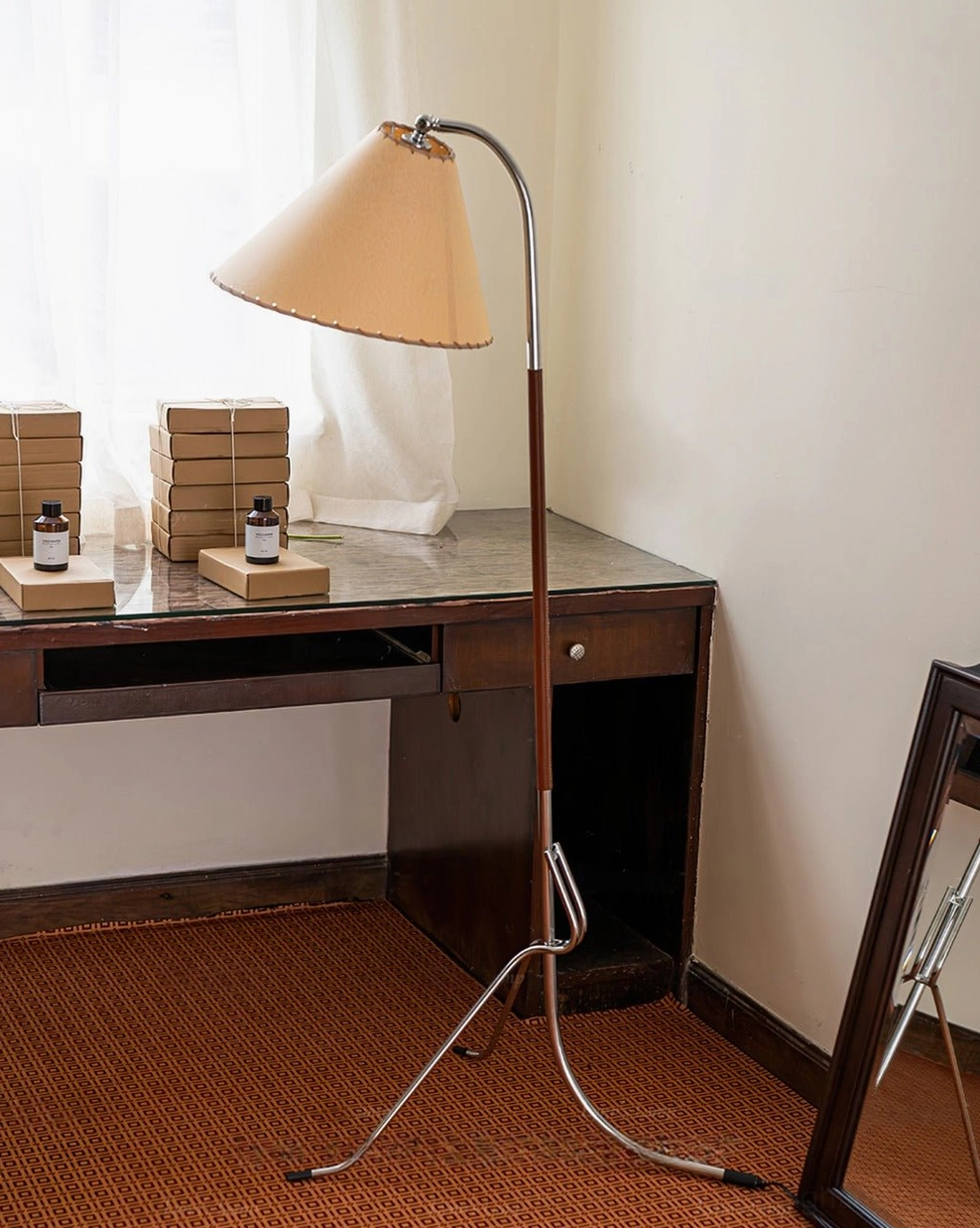 Tripod floor lamp side profile positioned near woven brown carpet and home decor with leaning floor mirror in living space