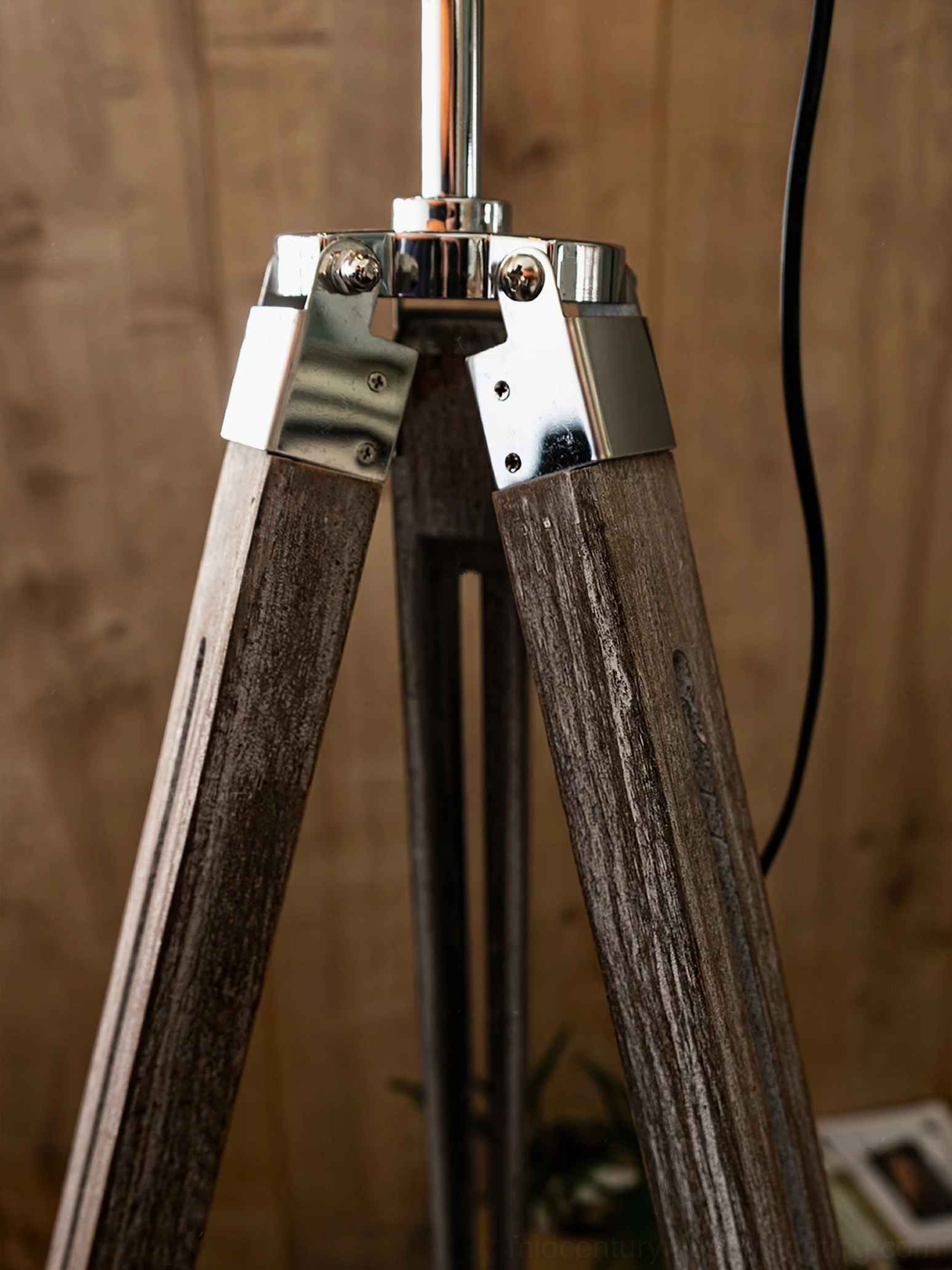 Close-up detail of industrial tripod lamp joint, polished chrome metal fasteners and natural wood grain on wooden wall background