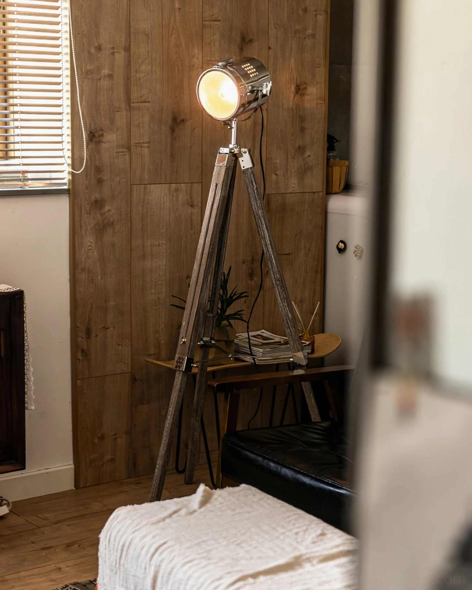 Chrome metal tripod floor lamp reflected in mirror, vintage living room setting, weathered wood legs and polished metal lamp head detail