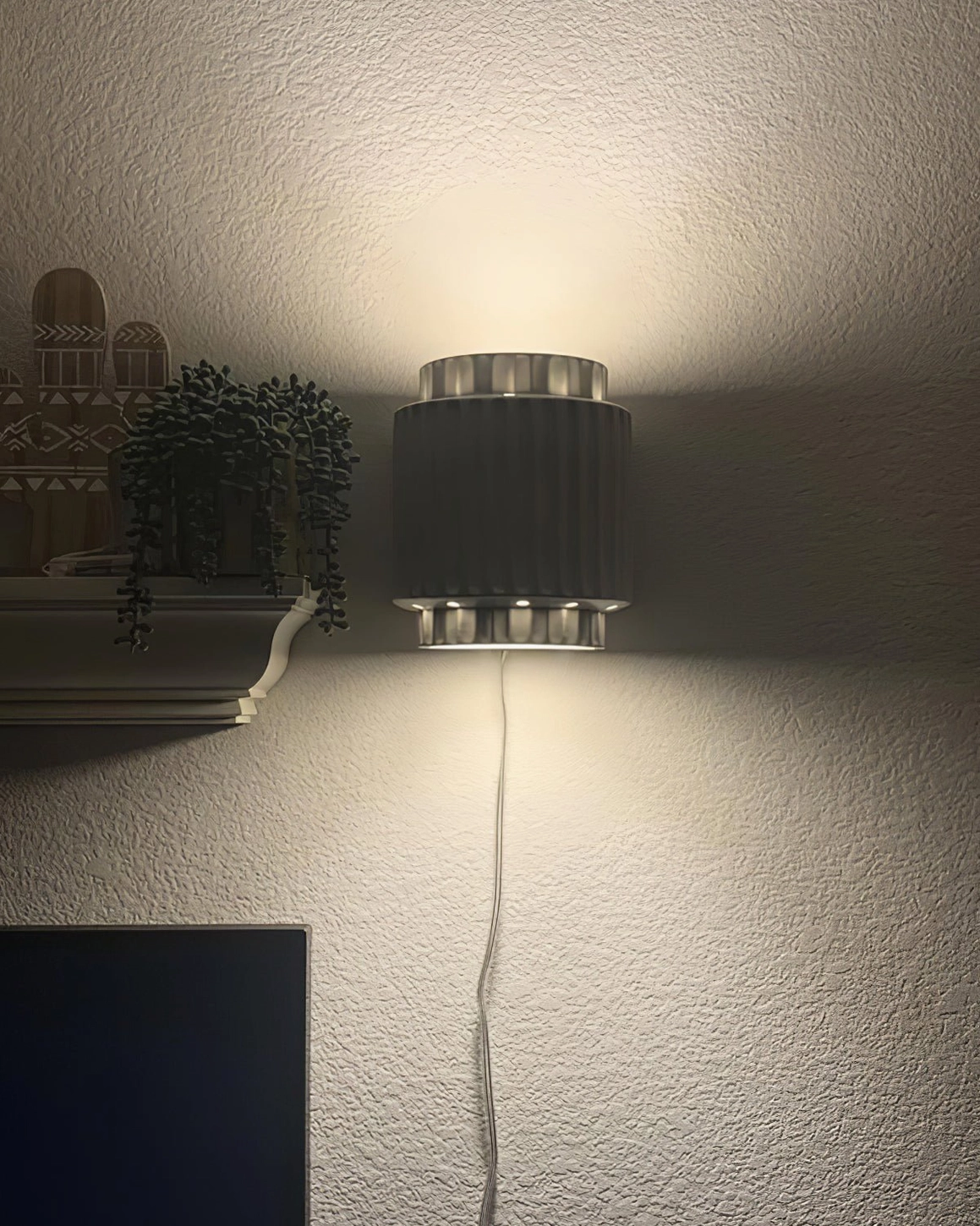 Modern Tristan cylinder wall sconce with upward lighting on textured accent wall in contemporary home interior