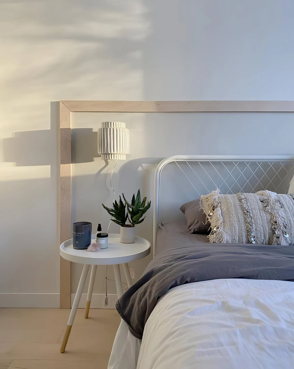 Tristan modern wall lamp installed in contemporary bedroom beside bed frame with minimalist nightstand and plant decor