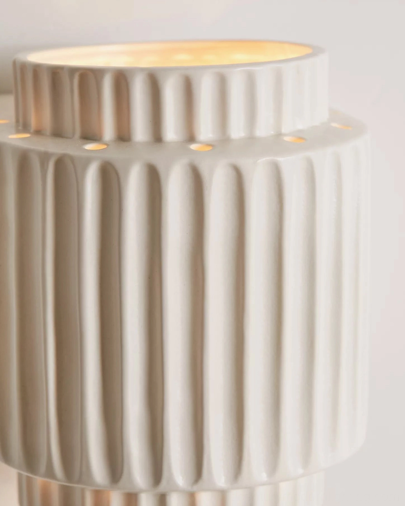 Close-up detail of Tristan sconce showing vertical fluted texture, perforated rim, and illuminated interior glow
