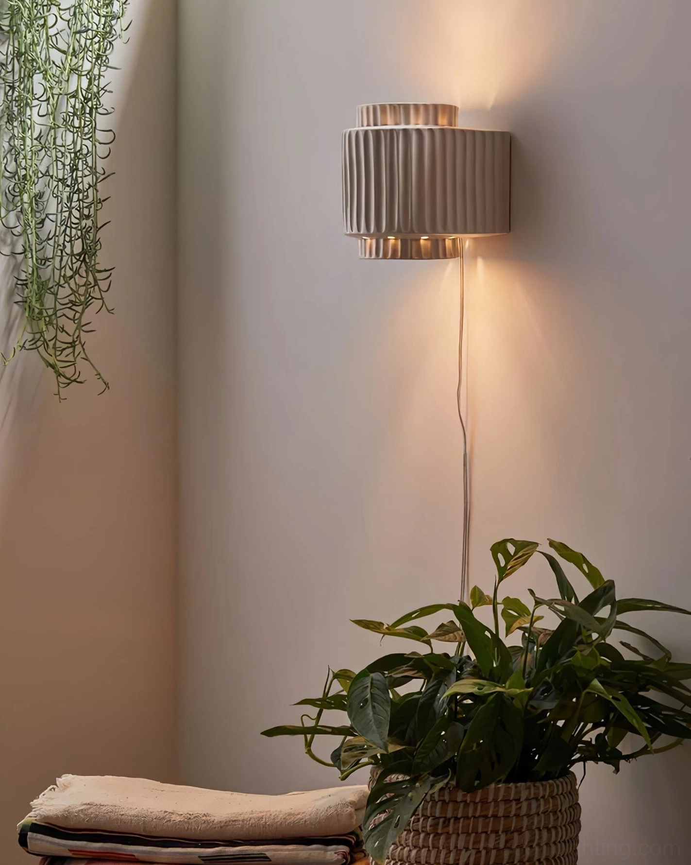 Matte white Tristan wall sconce creating warm ambient lighting in boho home corner with hanging plants and greenery