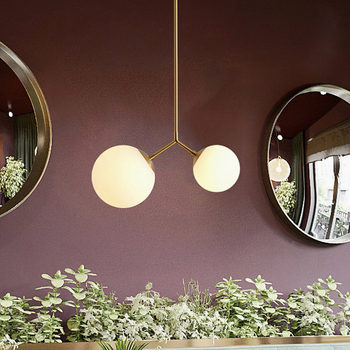 Twis asymmetric pendant lamp with brass frame and mixed glass shades styled above burgundy accent wall with decorative mirrors