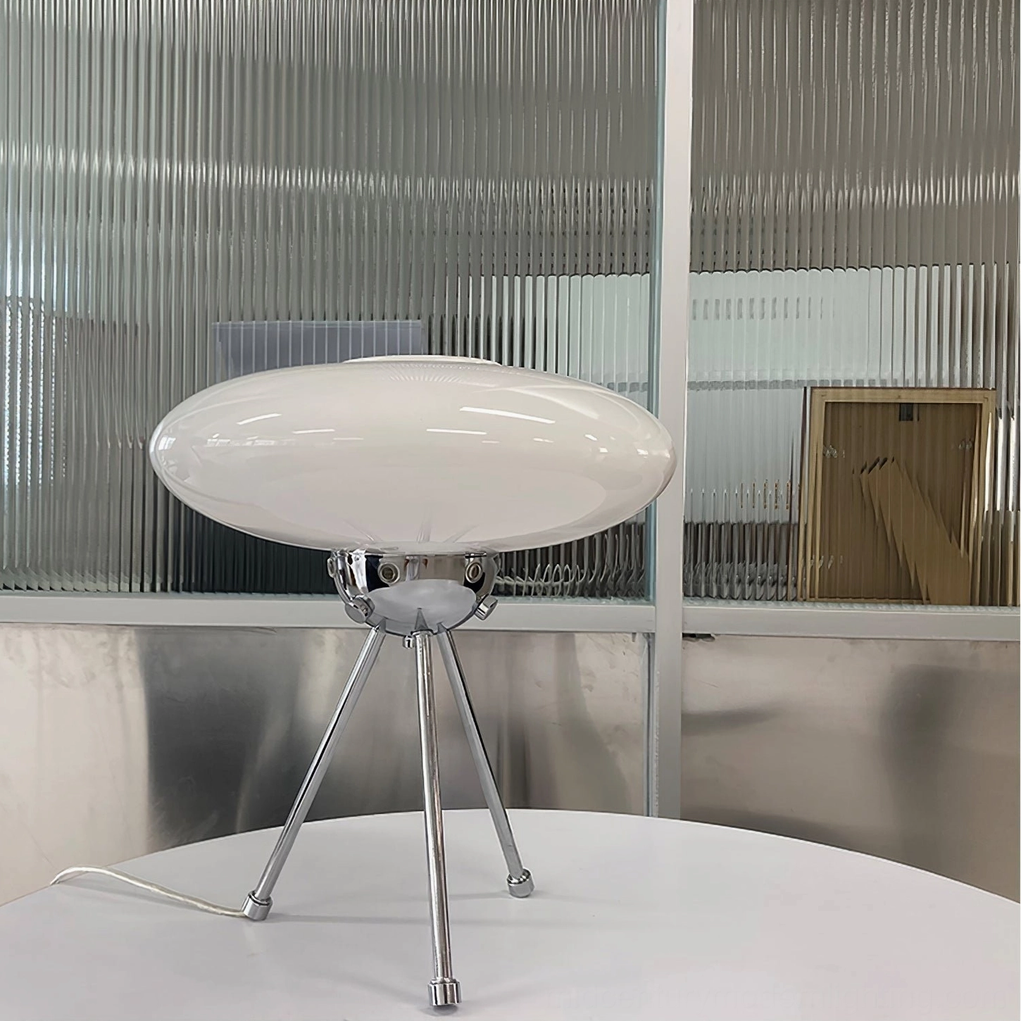 Frosted glass UFO dome lamp with silver chrome tripod on table with ribbed glass backdrop