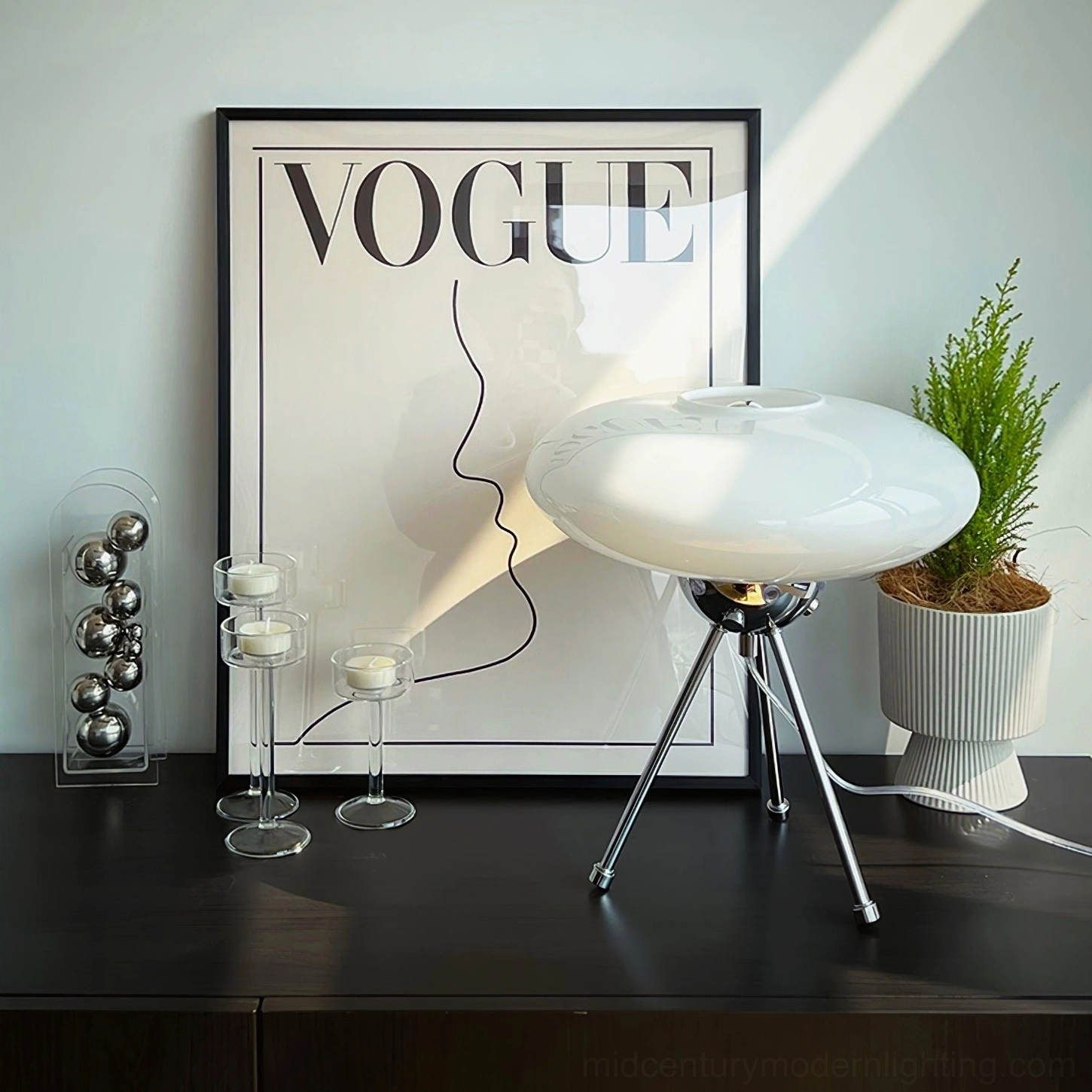 Chrome tripod UFO lamp on black dresser with Vogue poster and minimalist decor, 3/4 view