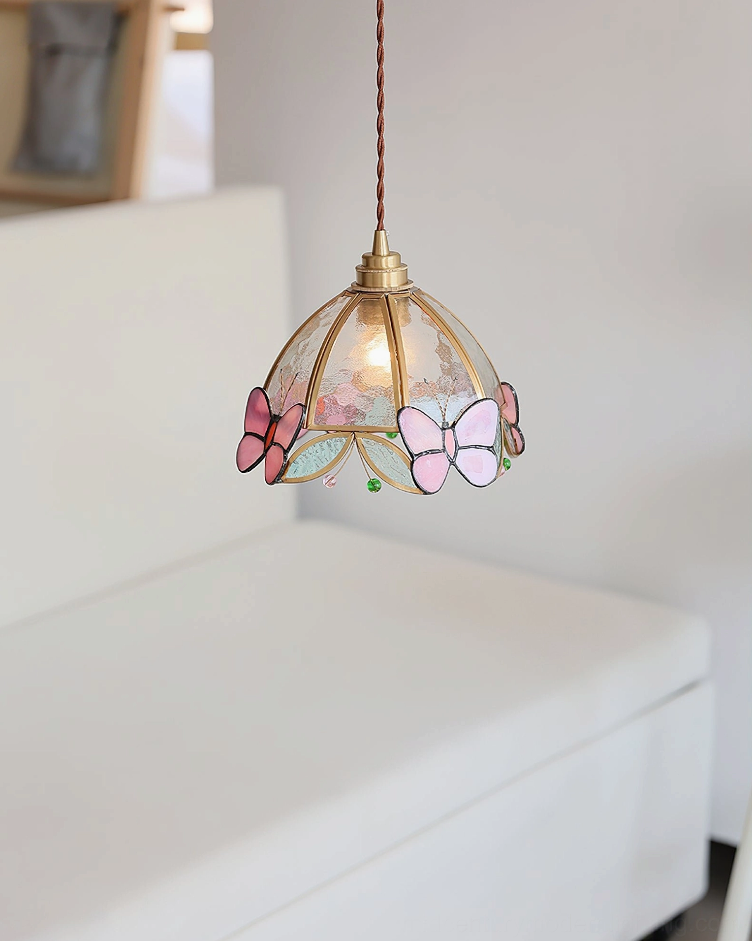 Three-quarter hanging perspective of Valinte pendant light with mixed pink butterfly decorations and soft warm ambient light in minimalist white sofa setting