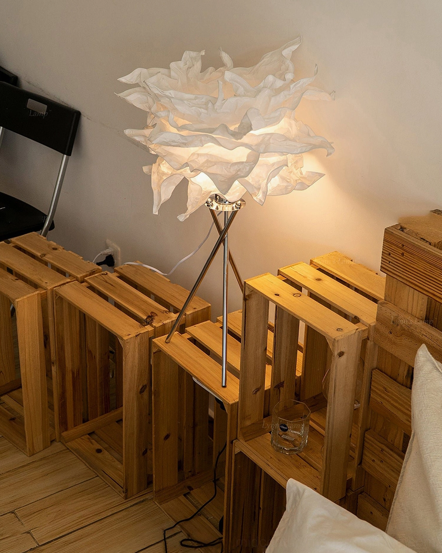 Veli cloud-inspired table lamp with visible power cord and chrome tripod legs displayed on wooden furniture, low angle three-quarter view