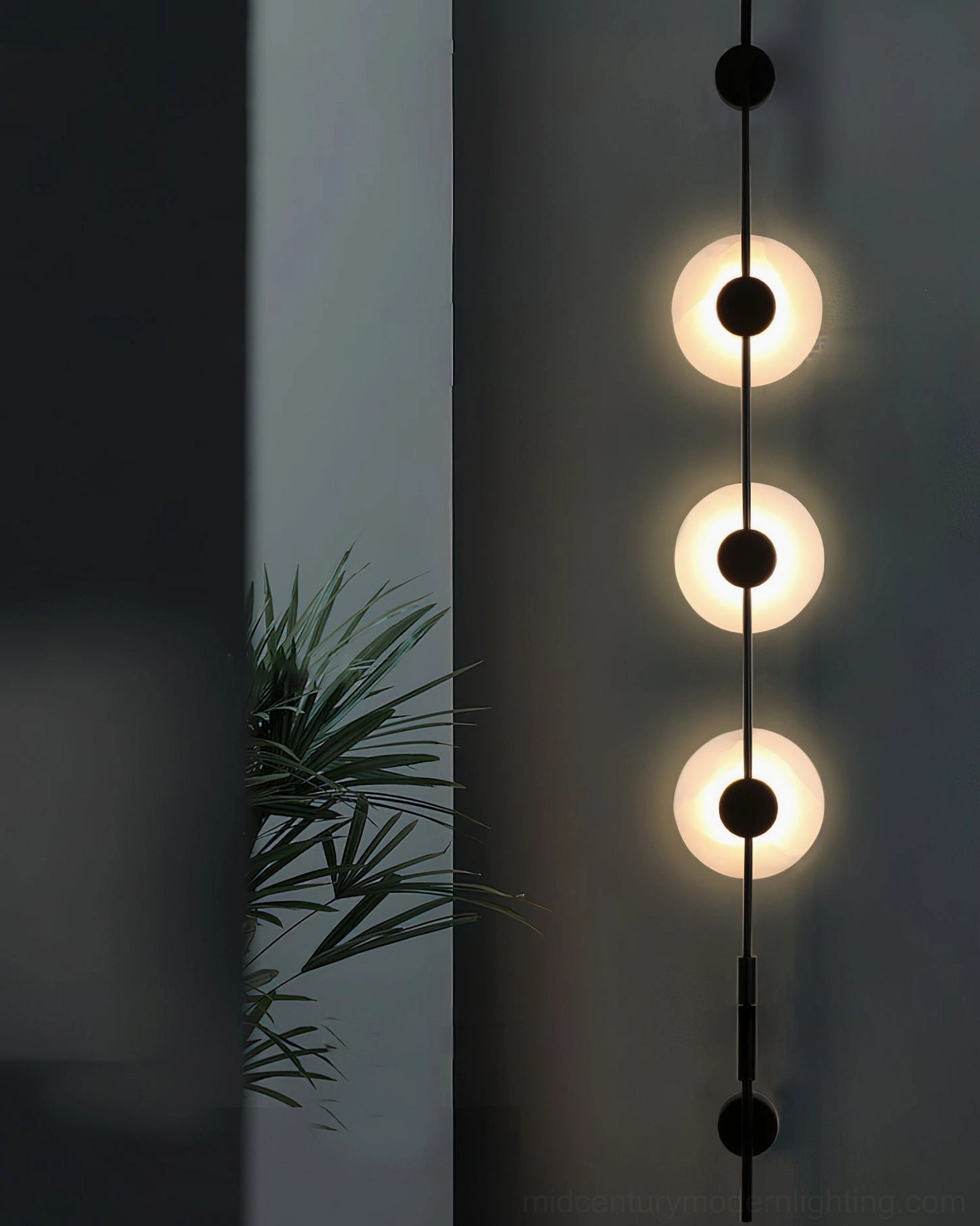 Close-up detail of three-light vertical alabaster wall lamp in matte black with illuminated circular frosted alabaster covers