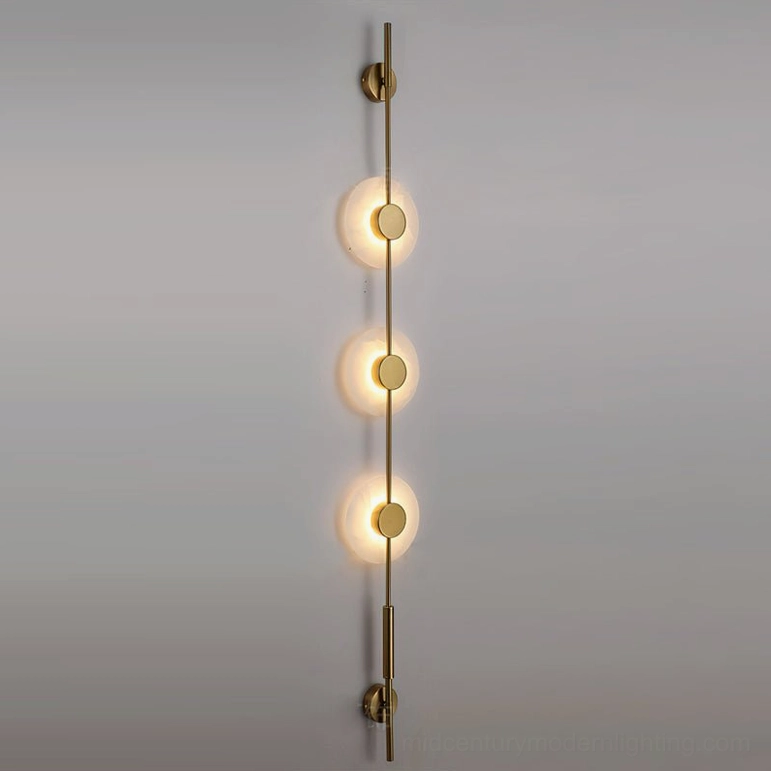 Three-light vertical alabaster wall lamp with warm gold metallic finish on gray studio background displaying elegance and scale