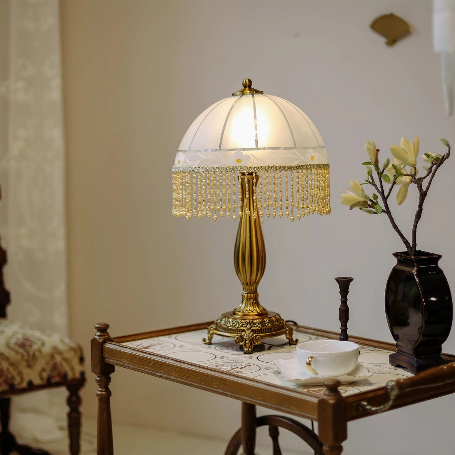 Decorative brass tassel lamp positioned on vintage side table with black vase and antique wooden chair