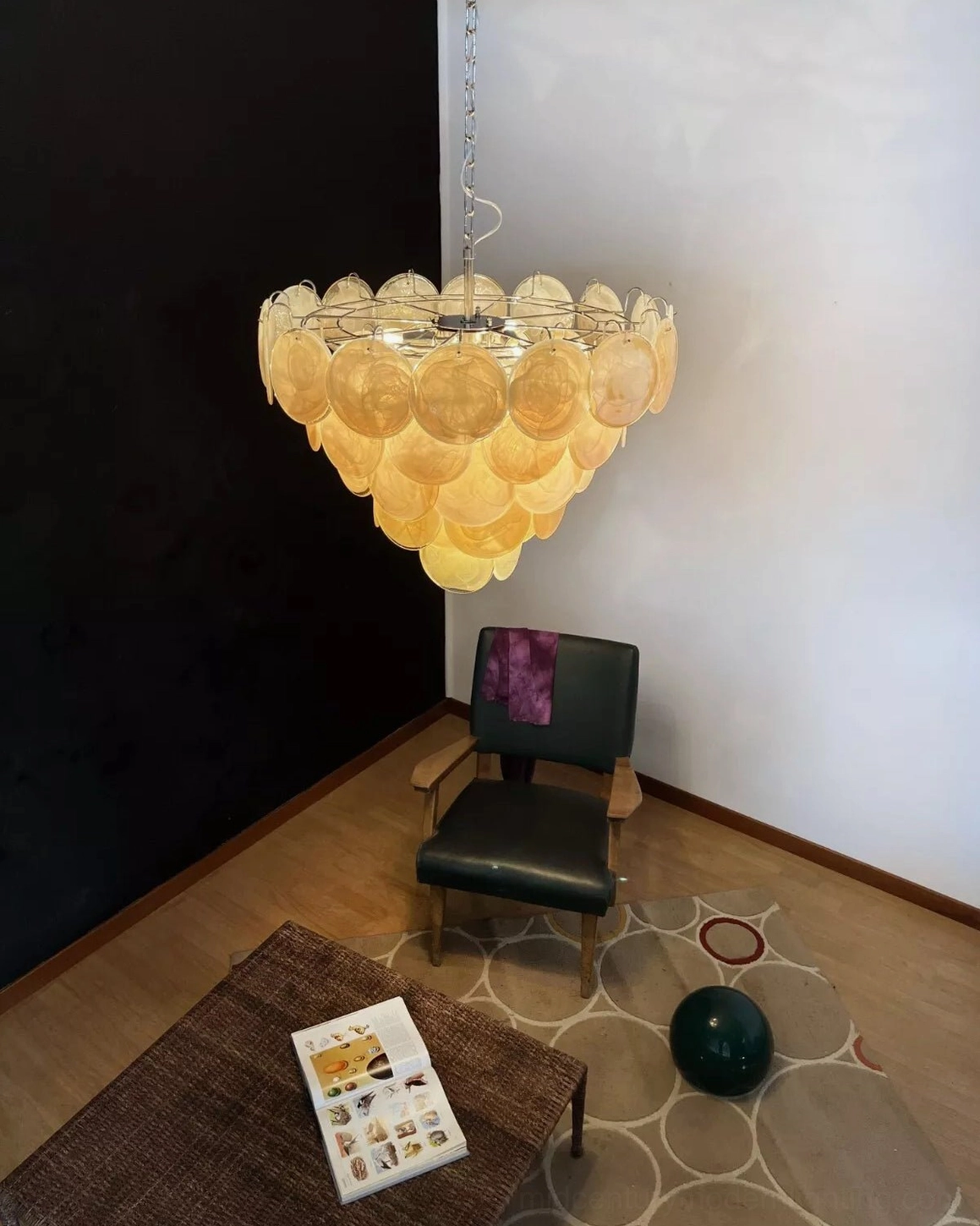 Side angle view of tiered glass chandelier in residential sitting area with brown coffee table and wood flooring