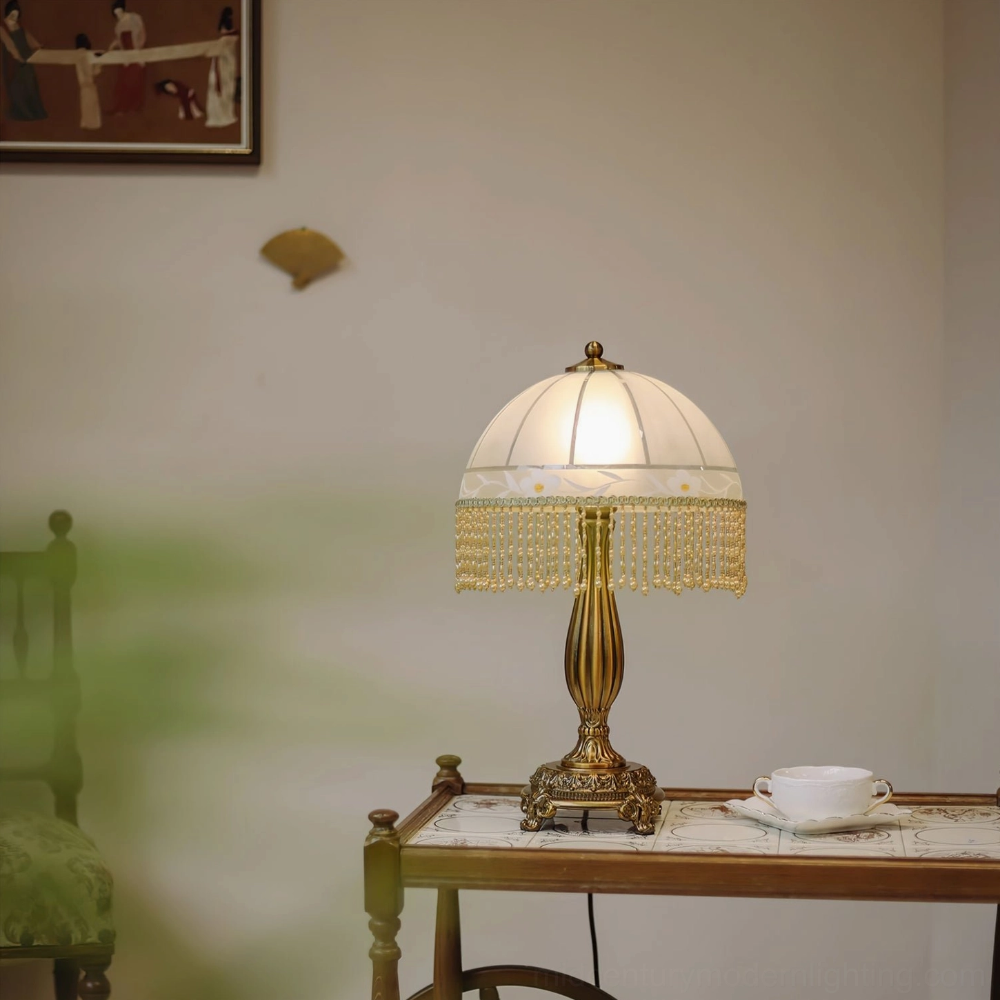 Brass tassel flower table lamp beside tea set on vintage wooden table with antique chair backdrop