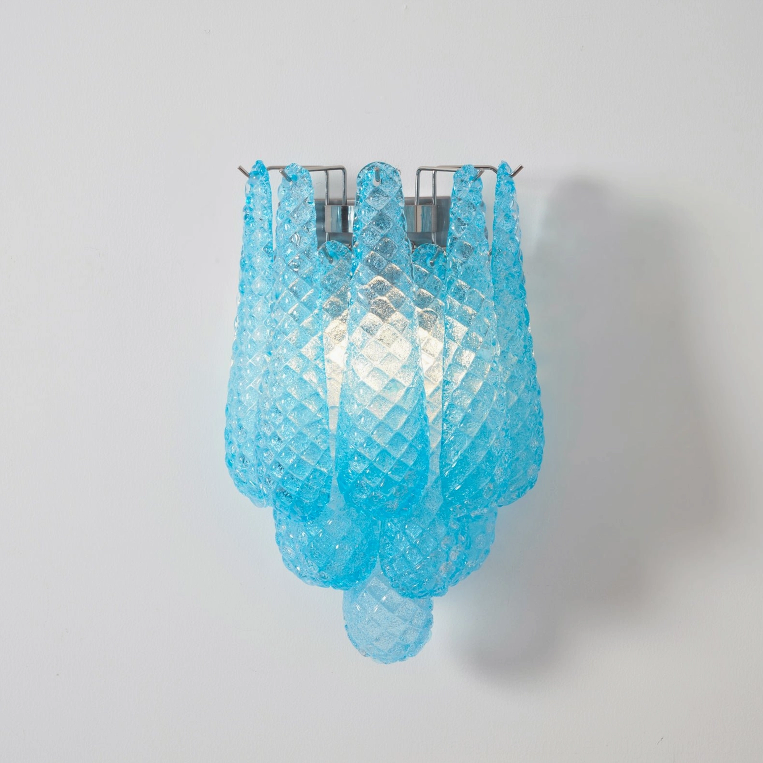 Blue textured Murano glass Viola Drop wall sconce glowing brightly in close-up view
