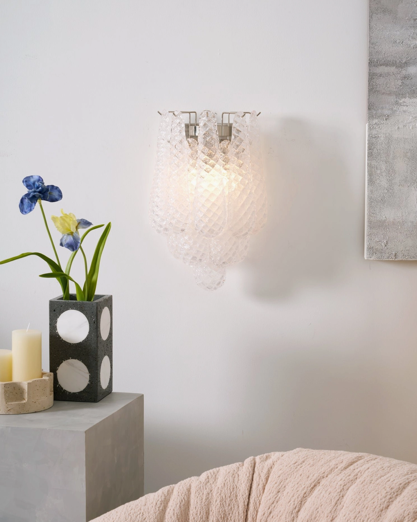 Illuminated clear Viola Drop sconce creating soft light with floral home decor arrangement