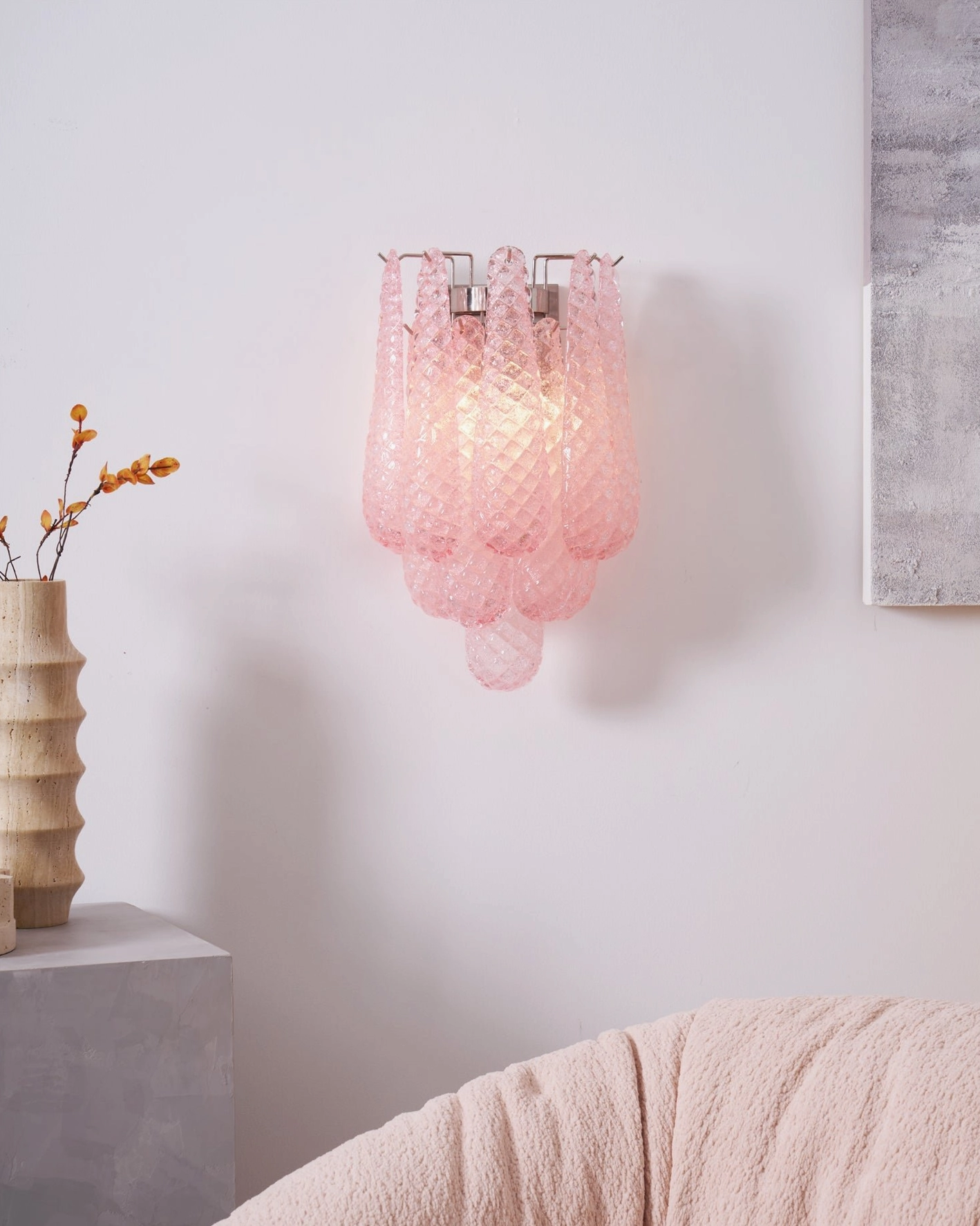 Illuminated pink Viola Drop glass sconce in cozy bedroom setting with pink sofa accent