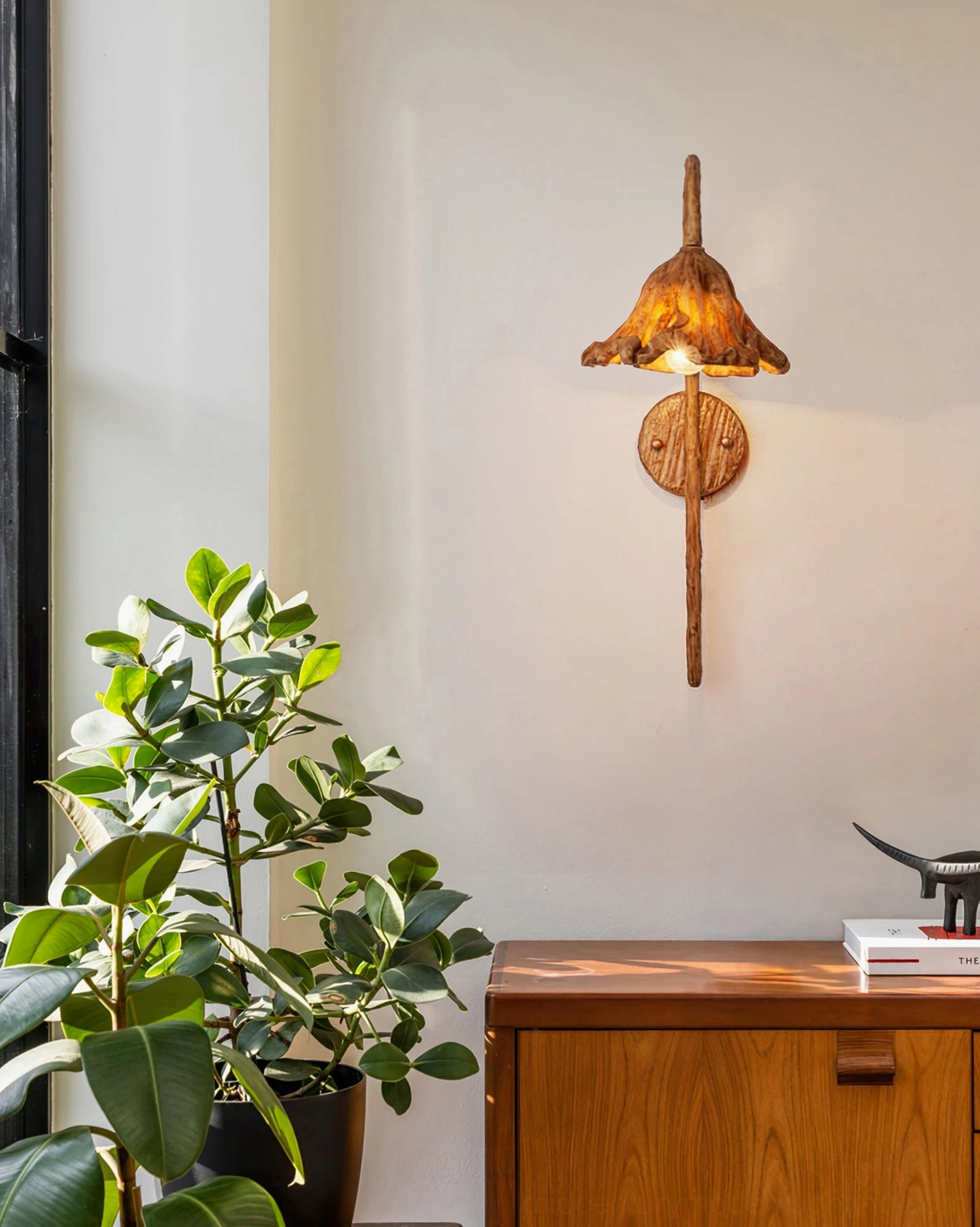 Volcano wall lamp in residential entryway mounted beside wooden cabinet with green potted plant, warm ambient lighting