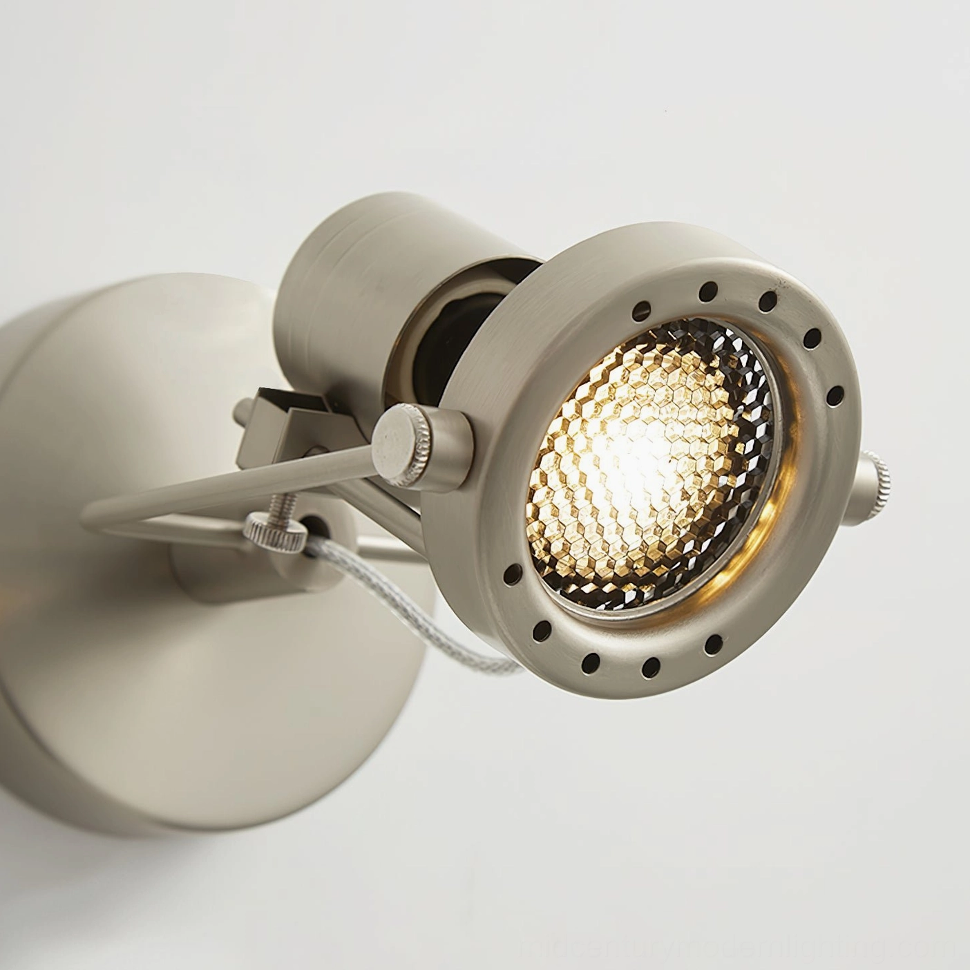 Overhead close-up of adjustable wall light showing large illuminated lamp bead and brass adjustment knobs