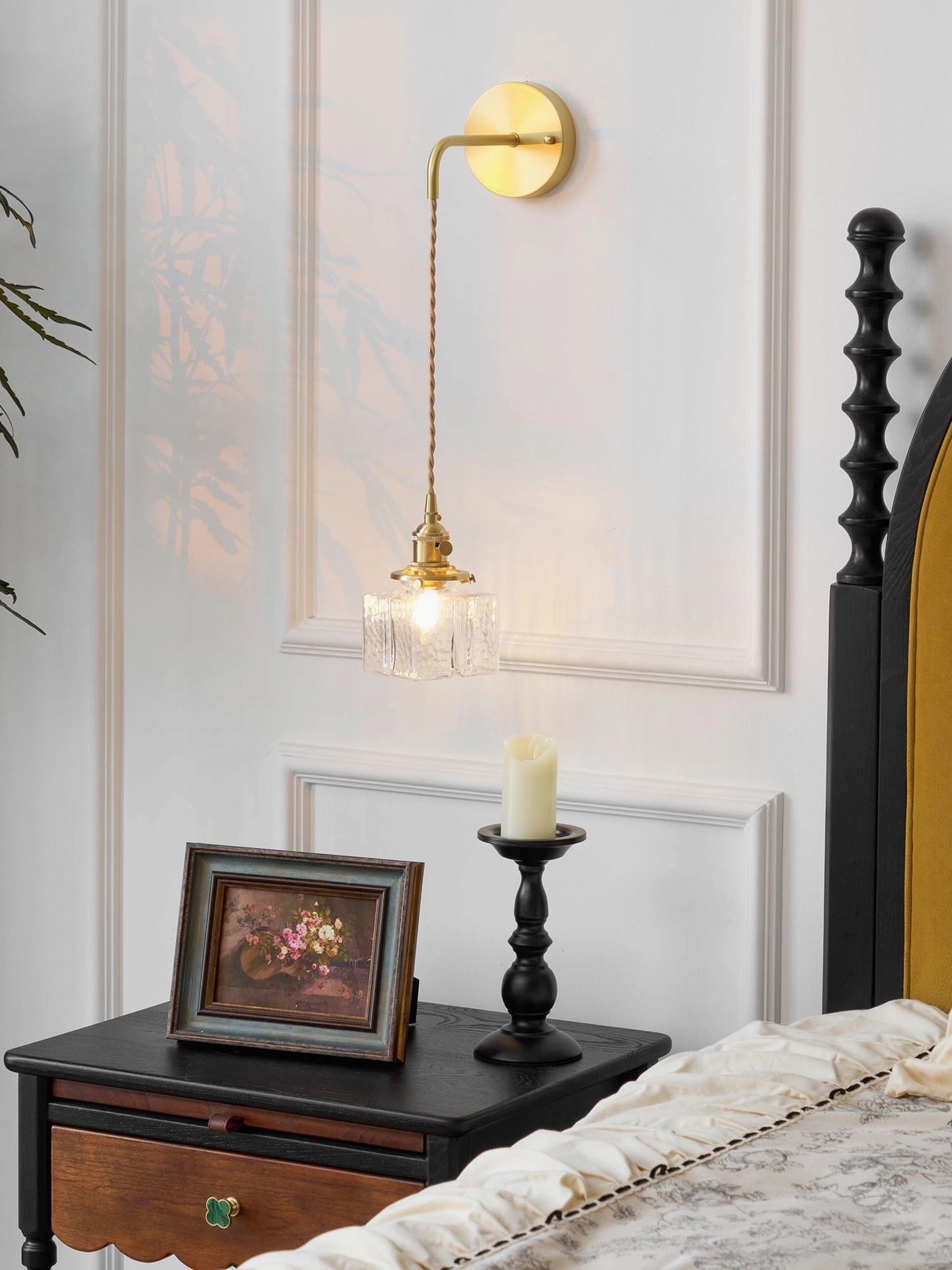 Warm vintage brass wall lamp with small textured glass shade in bedroom with nightstand