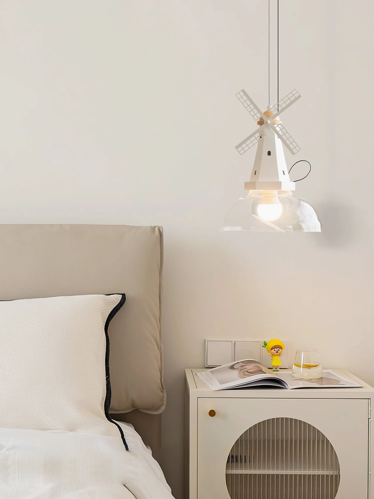 Windmill geometric pendant suspended in minimalist bedroom above small storage cabinet