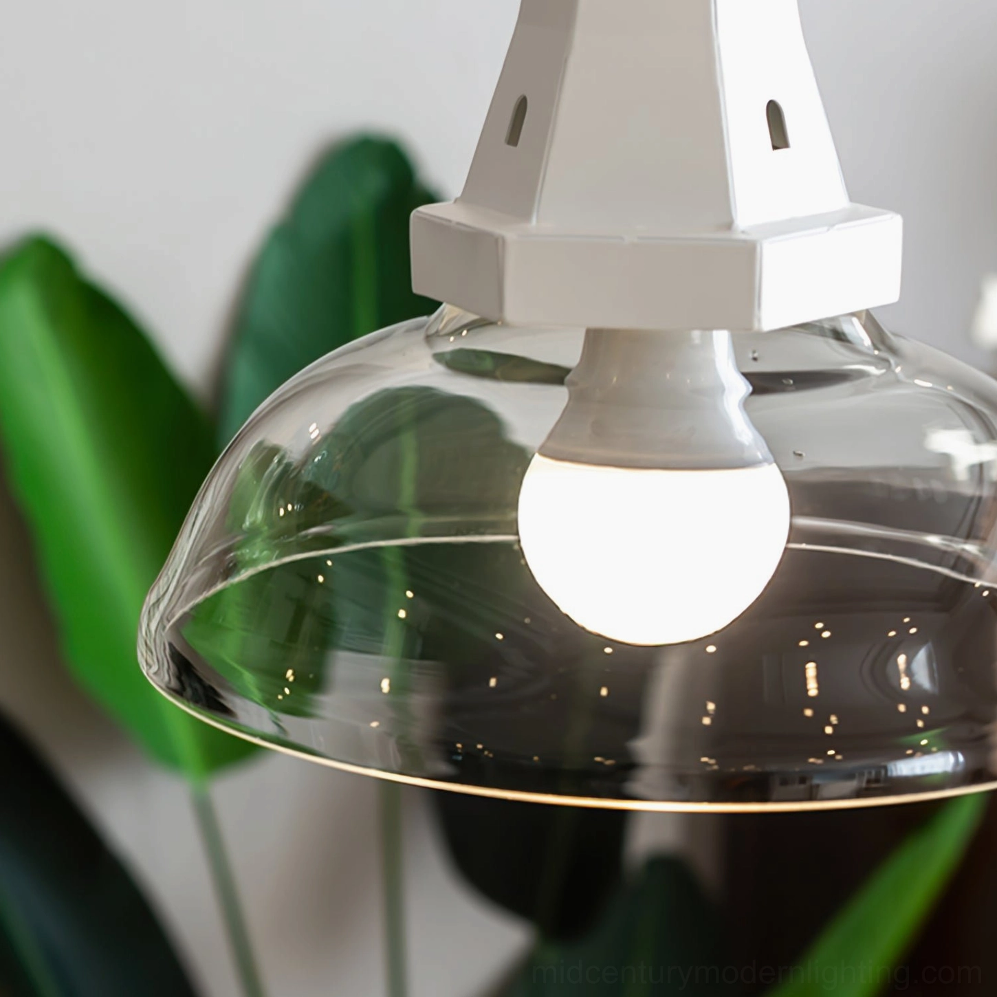 Bottom view of windmill pendant light showing exposed LED bulb and clear dome glass shade with tropical backdrop