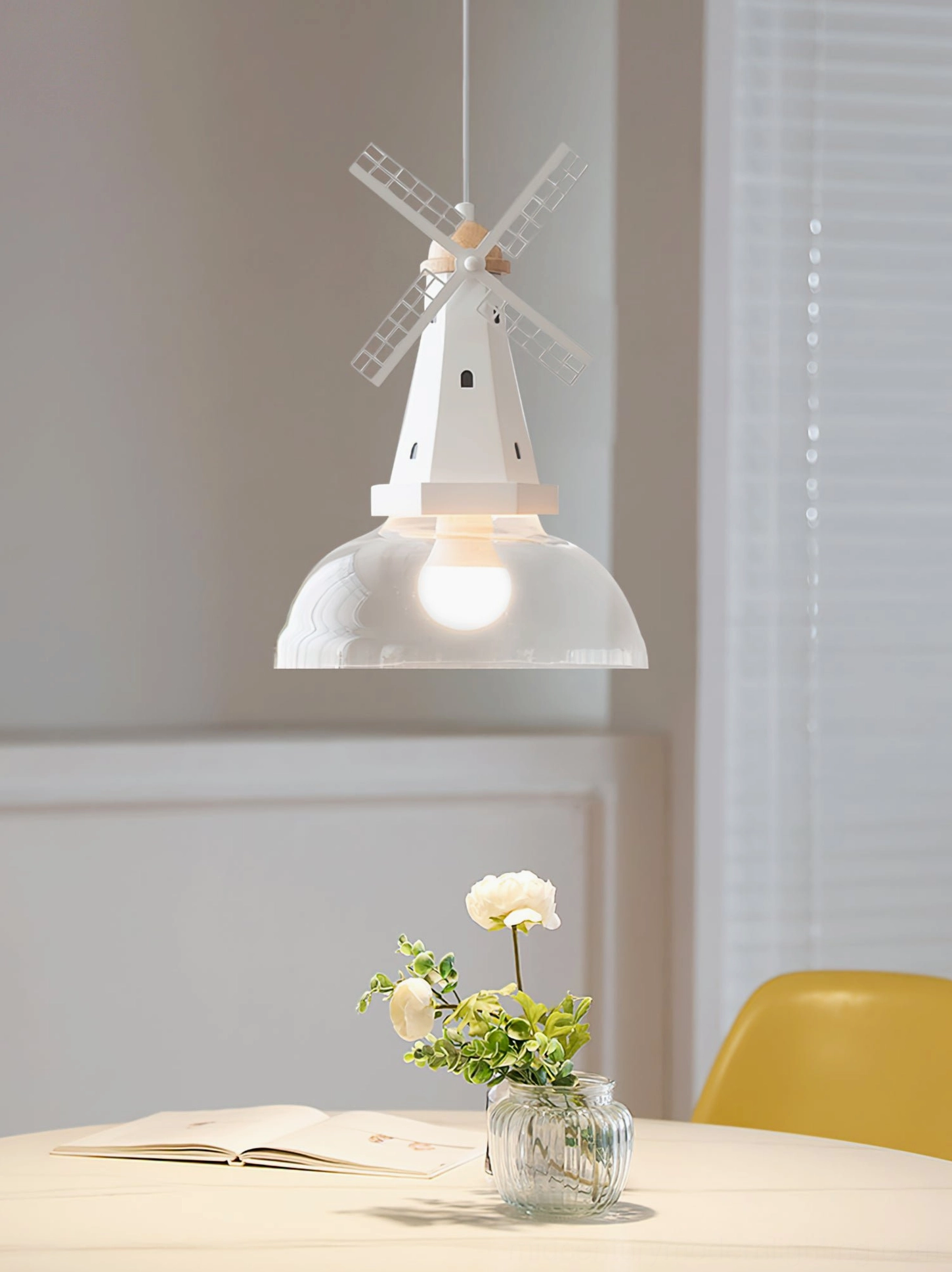 Windmill pendant light above dining table with floral centerpiece and yellow chair contemporary setting