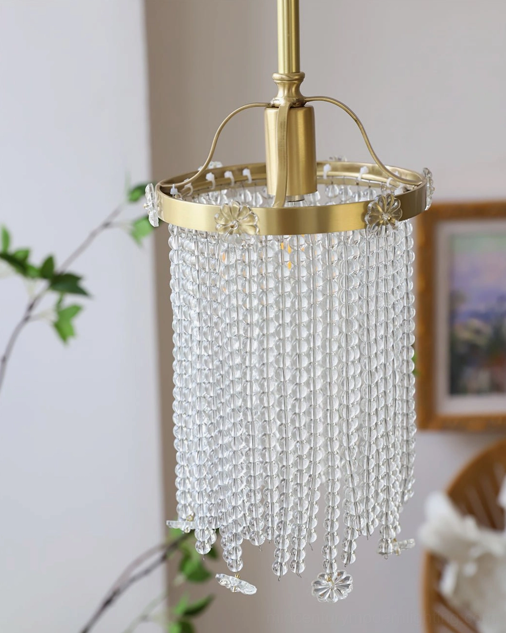 Winham crystal brass pendant lamp hanging in residential interior with green plants and wall art, mid-century modern styling