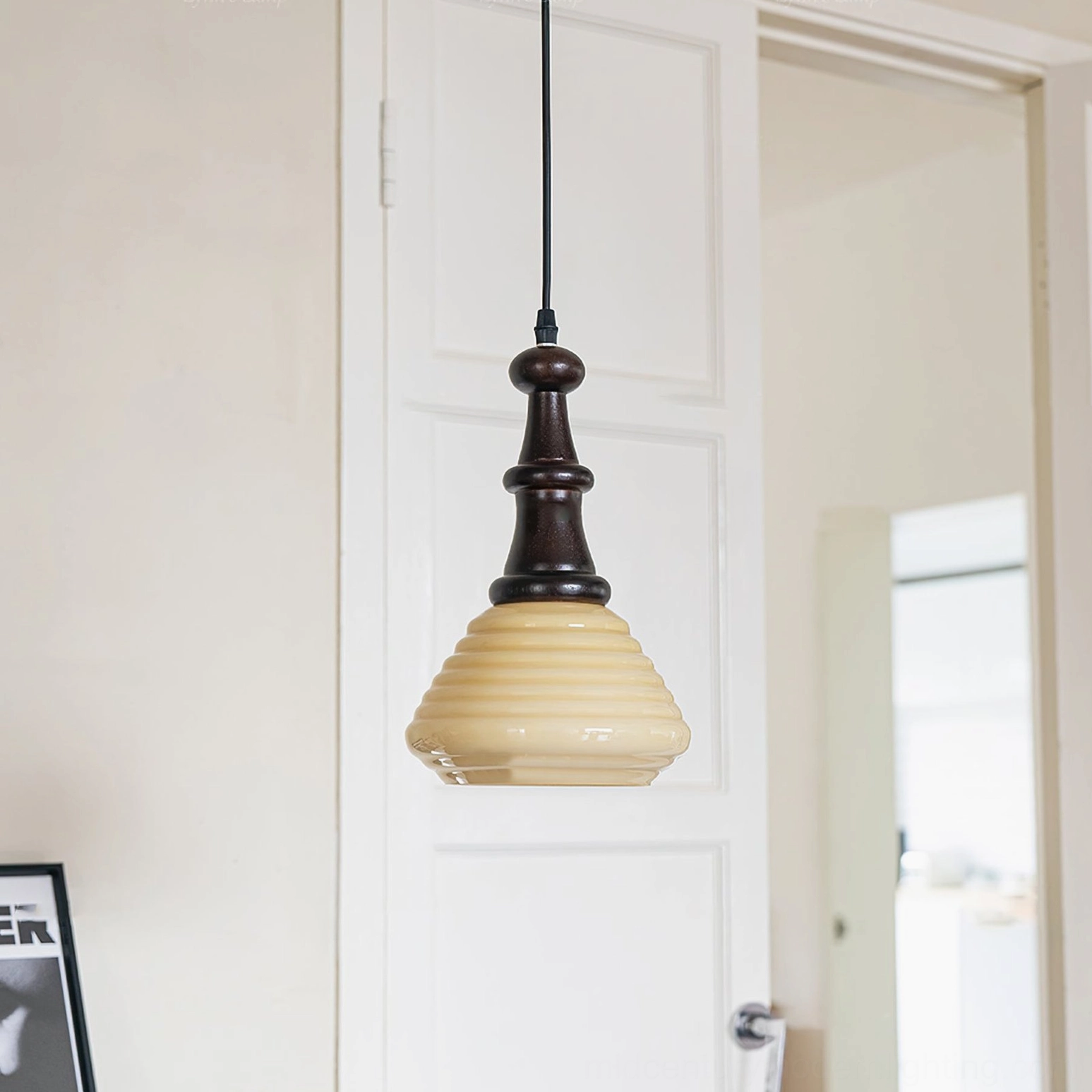 Wooden pendant light installed in modern home entryway with warm yellow illumination and black hanging cord, side angle view