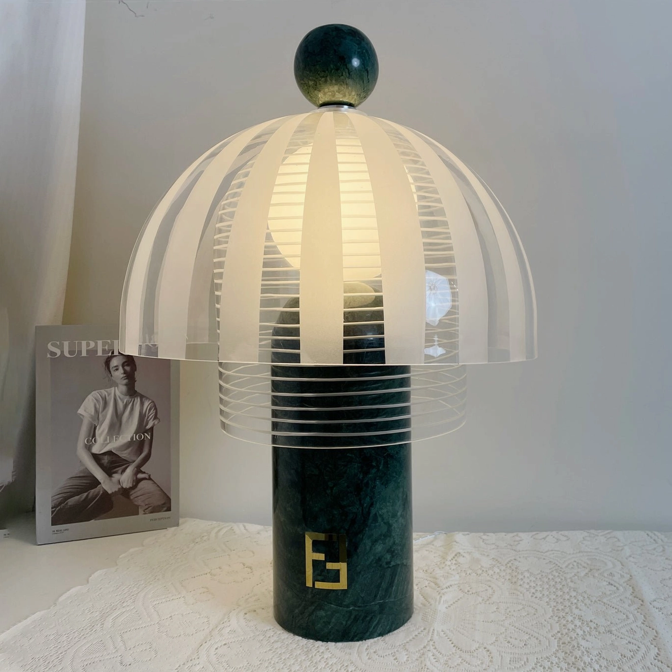 Illuminated Yasuke lamp on lace tablecloth with fashion magazine, three-quarter front perspective