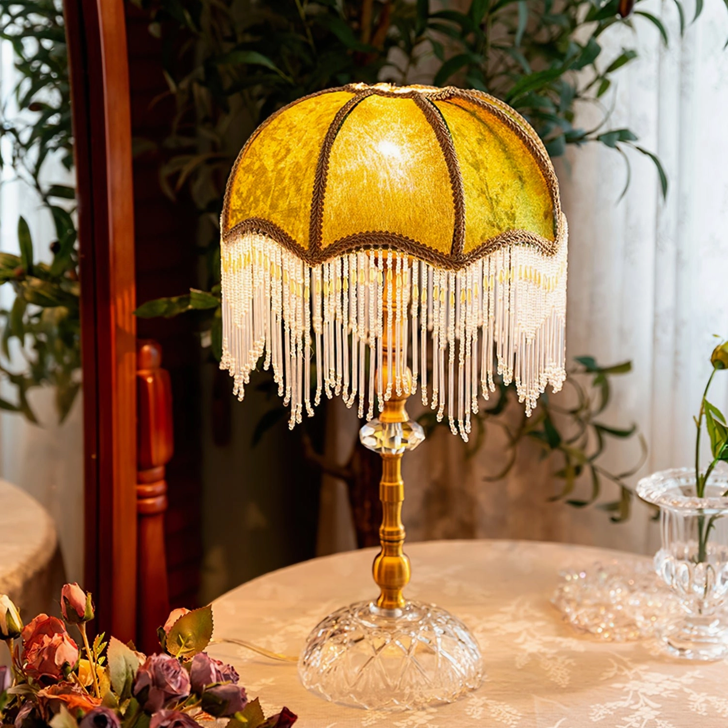Yellow shade fringed table lamp with brass and crystal base on indoor vintage tea table