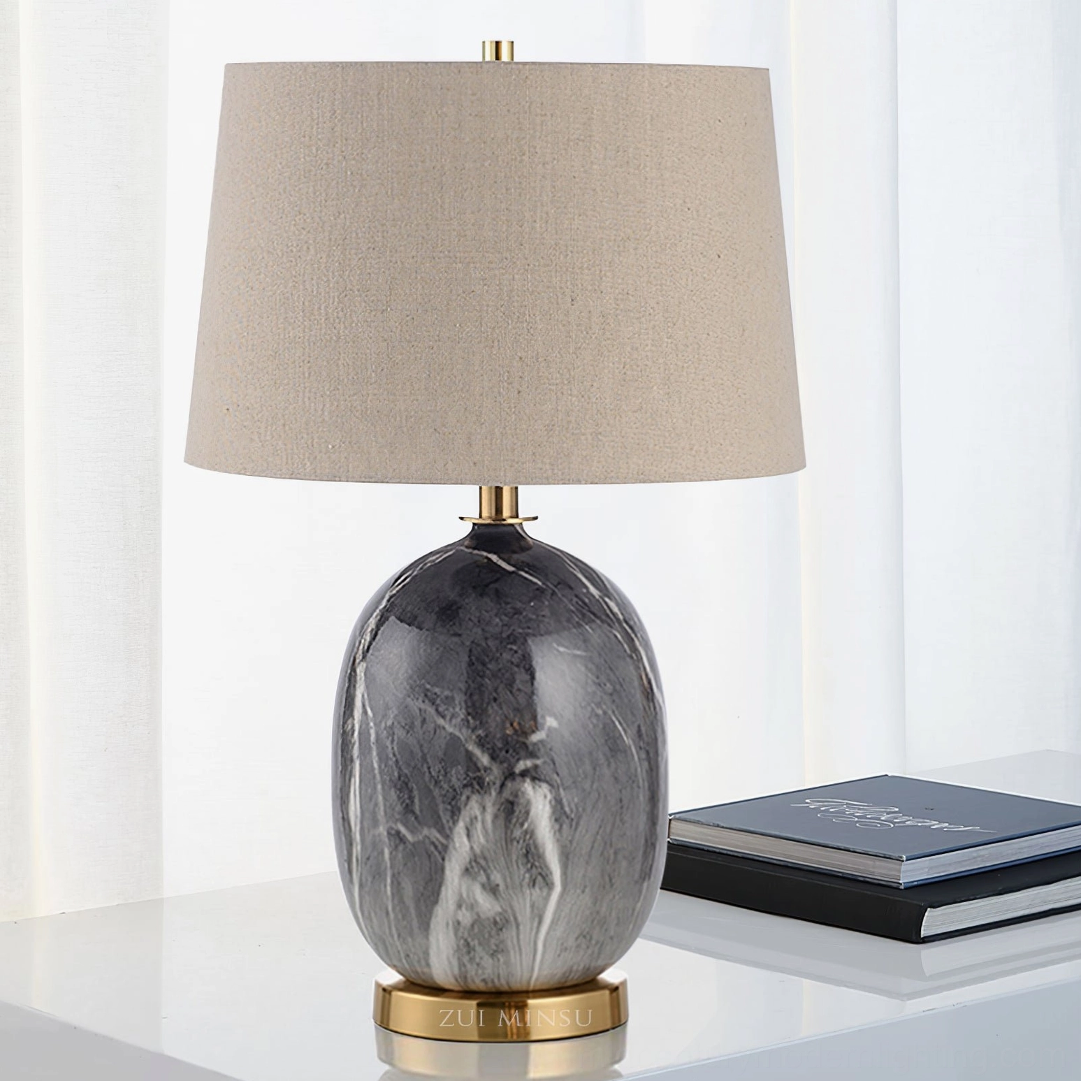 Dark grey marble table lamp with brass base on glass side table surrounded by books